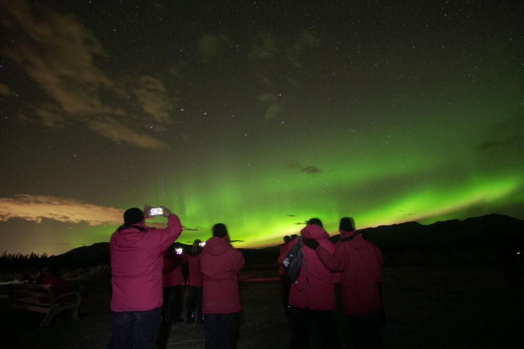 Grupo de viajeros tomando fotografías de auroras boreales con sus cámaras de teléfono